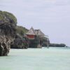 Thatched hut on rocky cliffs at Mtende Beach Zanzibar with clear shallow ocean water and rugged coastline
