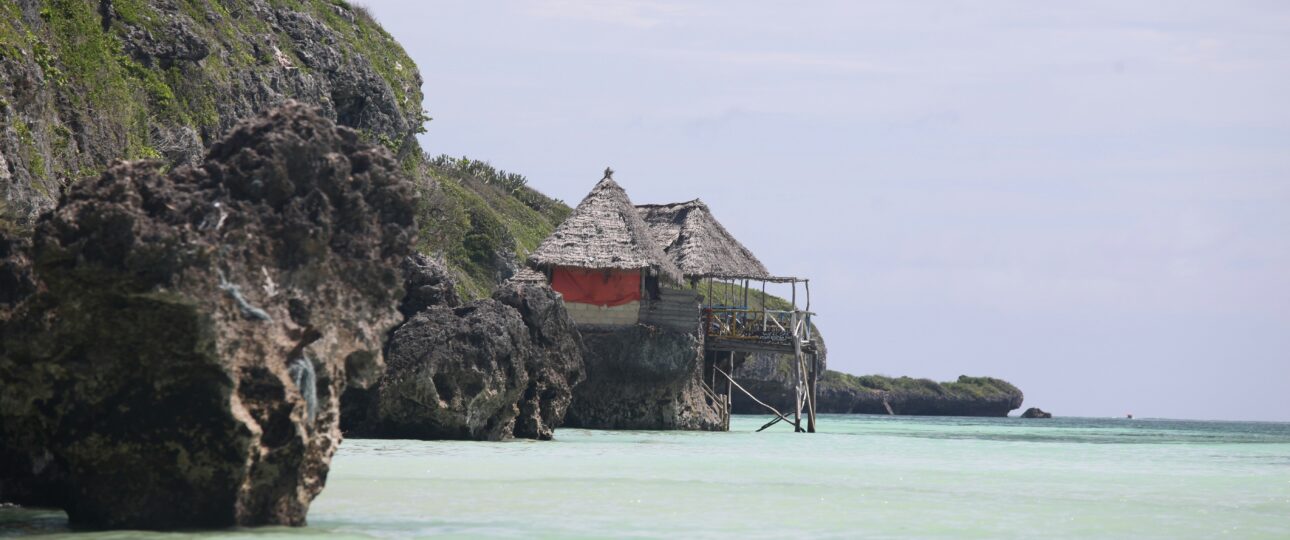 Thatched hut on rocky cliffs at Mtende Beach Zanzibar with clear shallow ocean water and rugged coastline
