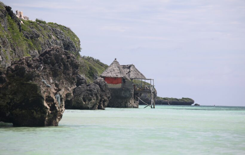 Thatched hut on rocky cliffs at Mtende Beach Zanzibar with clear shallow ocean water and rugged coastline