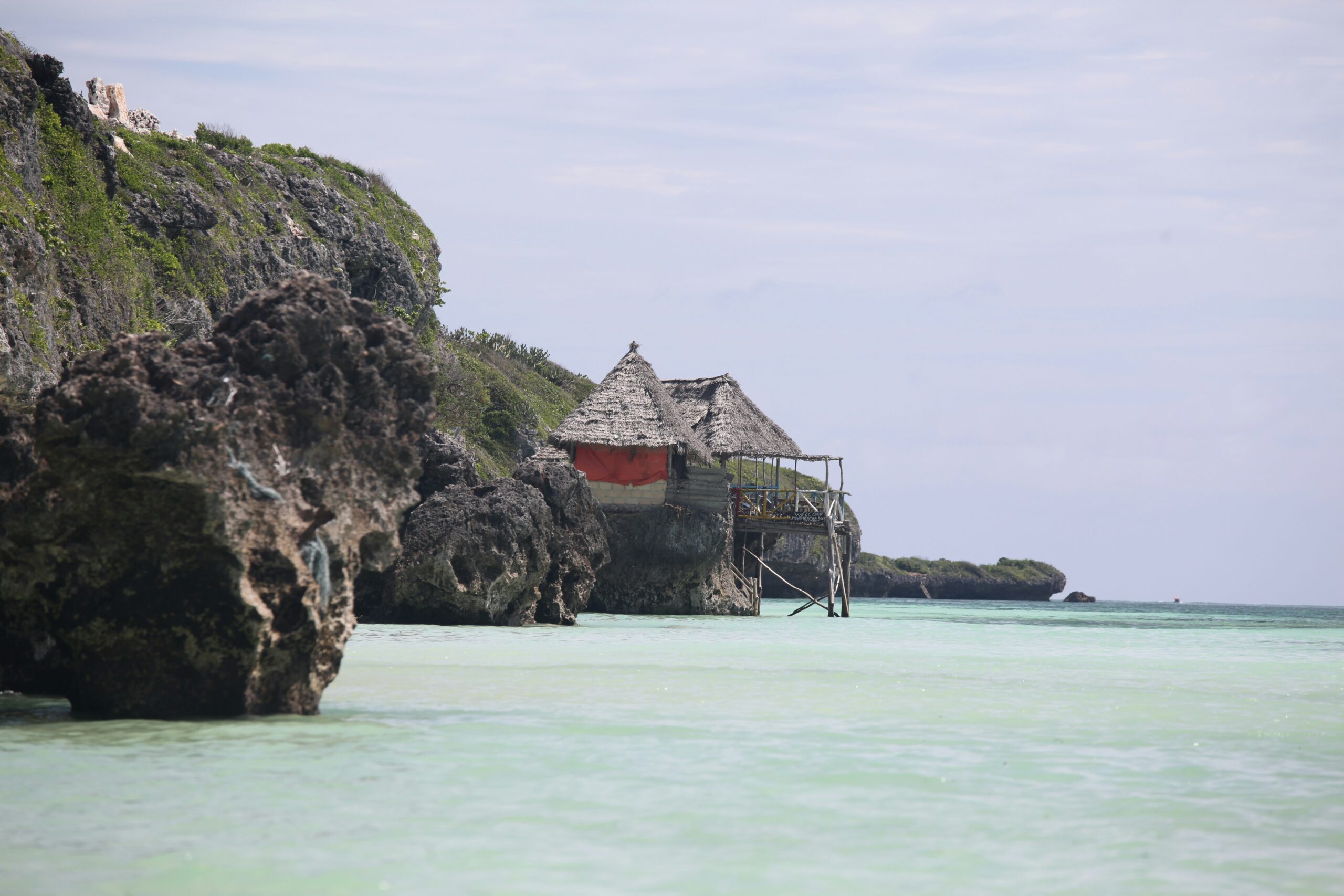 Thatched hut on rocky cliffs at Mtende Beach Zanzibar with clear shallow ocean water and rugged coastline