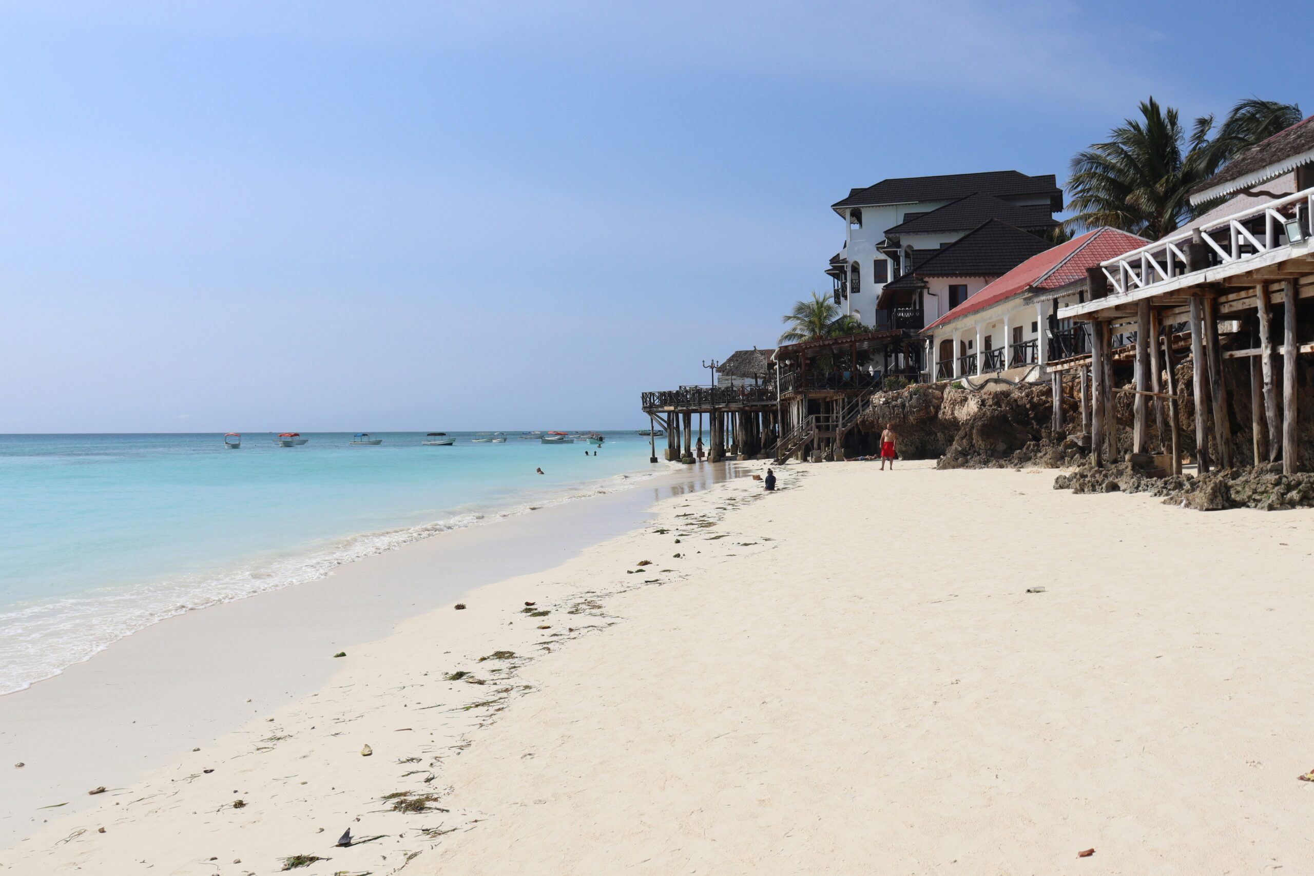 Nungwi Beach Zanzibar with white sand, turquoise ocean, wooden beachfront buildings, and boats near the shore