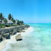 Zanzibar coastline with beach huts, palm trees, rocky shore, and clear turquoise ocean