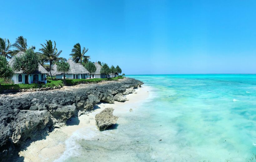 Zanzibar coastline with beach huts, palm trees, rocky shore, and clear turquoise ocean