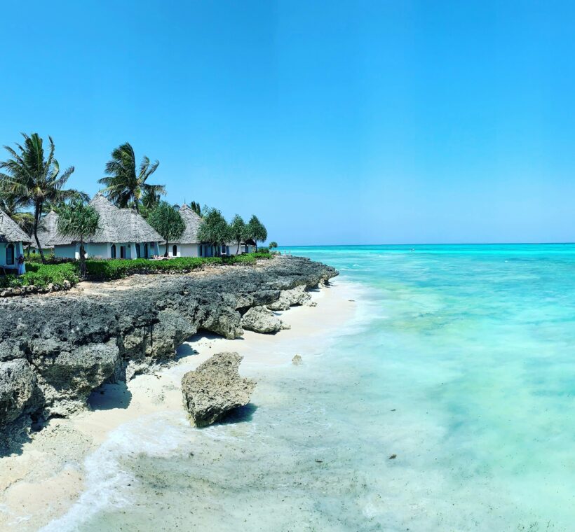Zanzibar coastline with beach huts, palm trees, rocky shore, and clear turquoise ocean