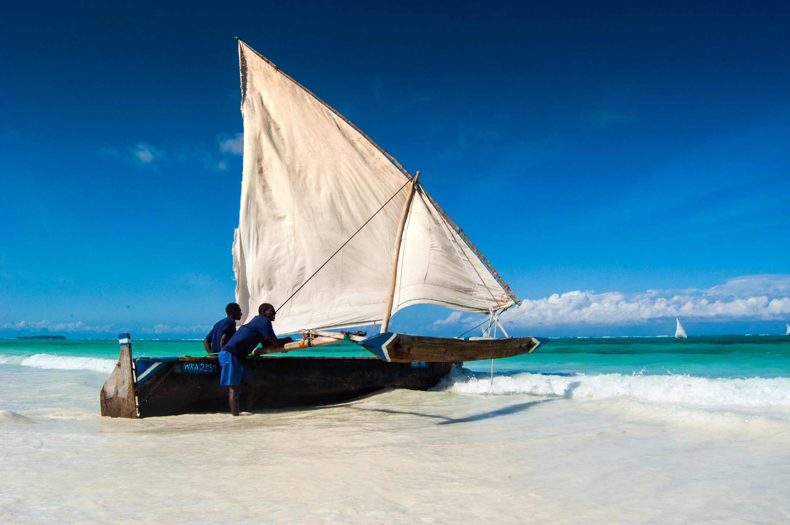 Zanzibar dhow boat with sail on turquoise water and white sand beach