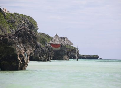 Thatched hut on rocky cliffs at Mtende Beach Zanzibar with clear shallow ocean water and rugged coastline